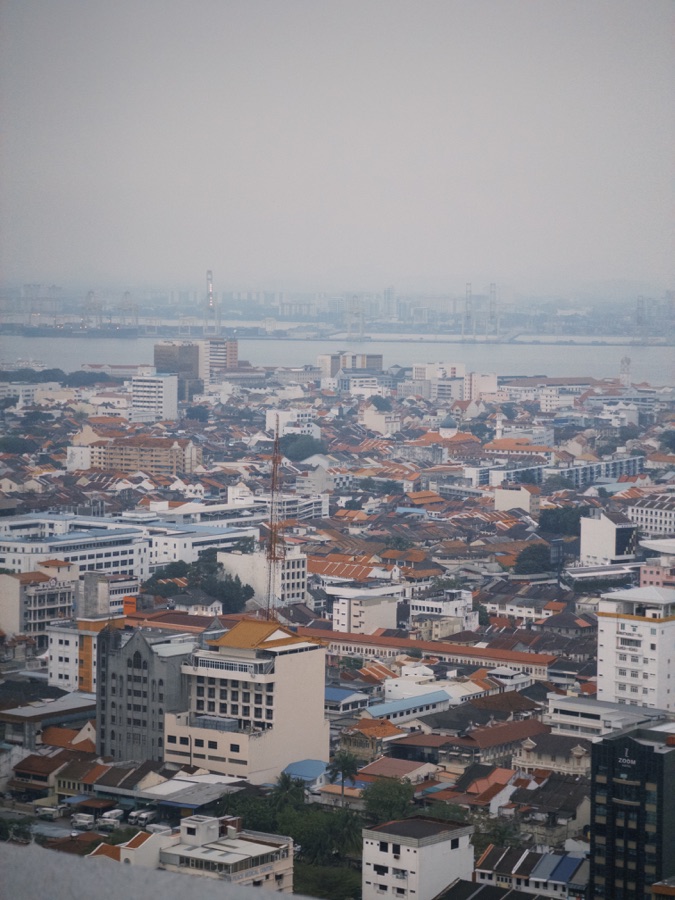Red rooftops and white buildings overlooking the water beneath a hazy sky.