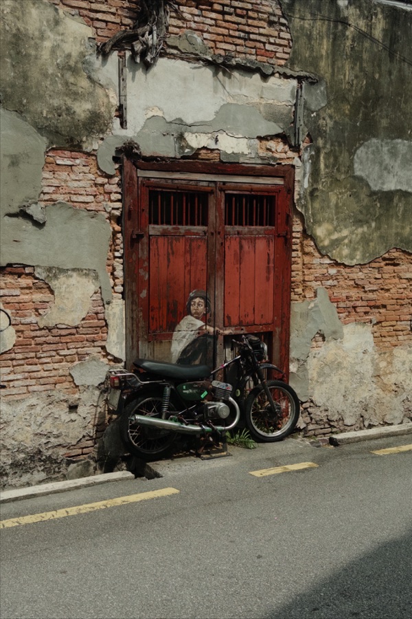 A motorcycle parked beside a red wooden door and a mural on a weathered brick wall.