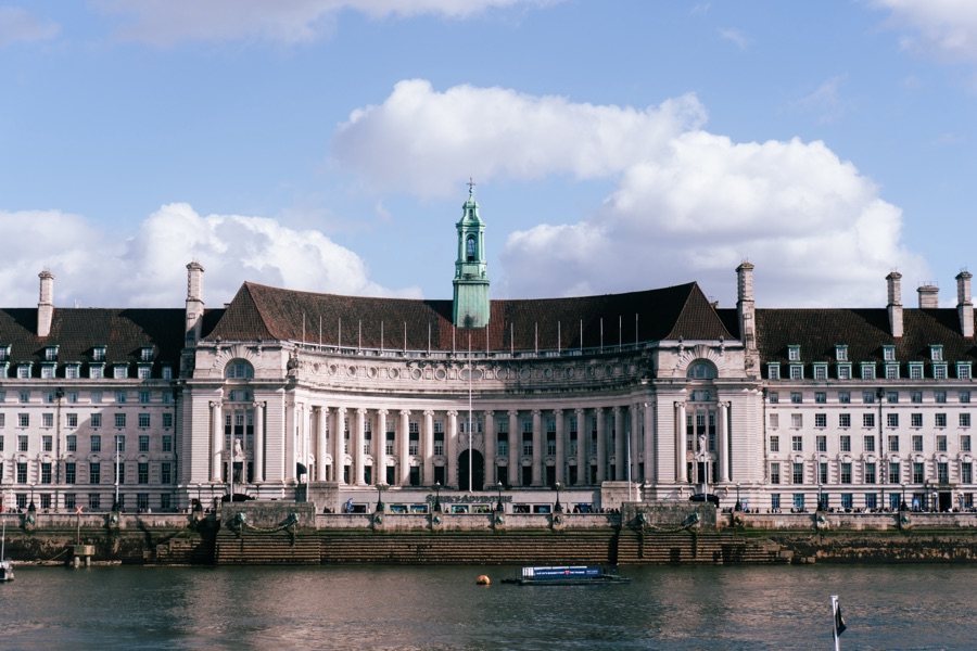 A grand riverside building with a green tower under scattered clouds.