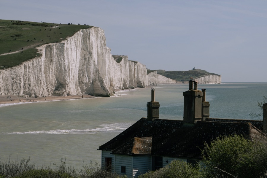 White chalk cliffs beside the sea, with a house in the foreground.