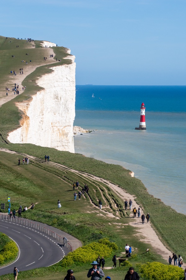 Walkers following paths along white cliffs with a red-and-white lighthouse offshore.