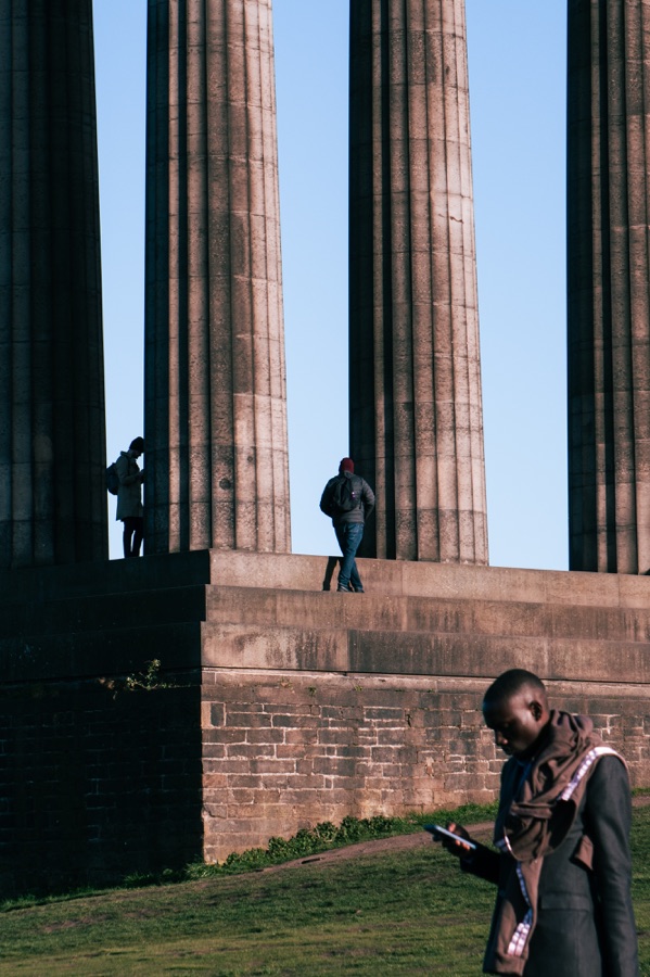 People standing between tall stone columns against a clear blue sky.